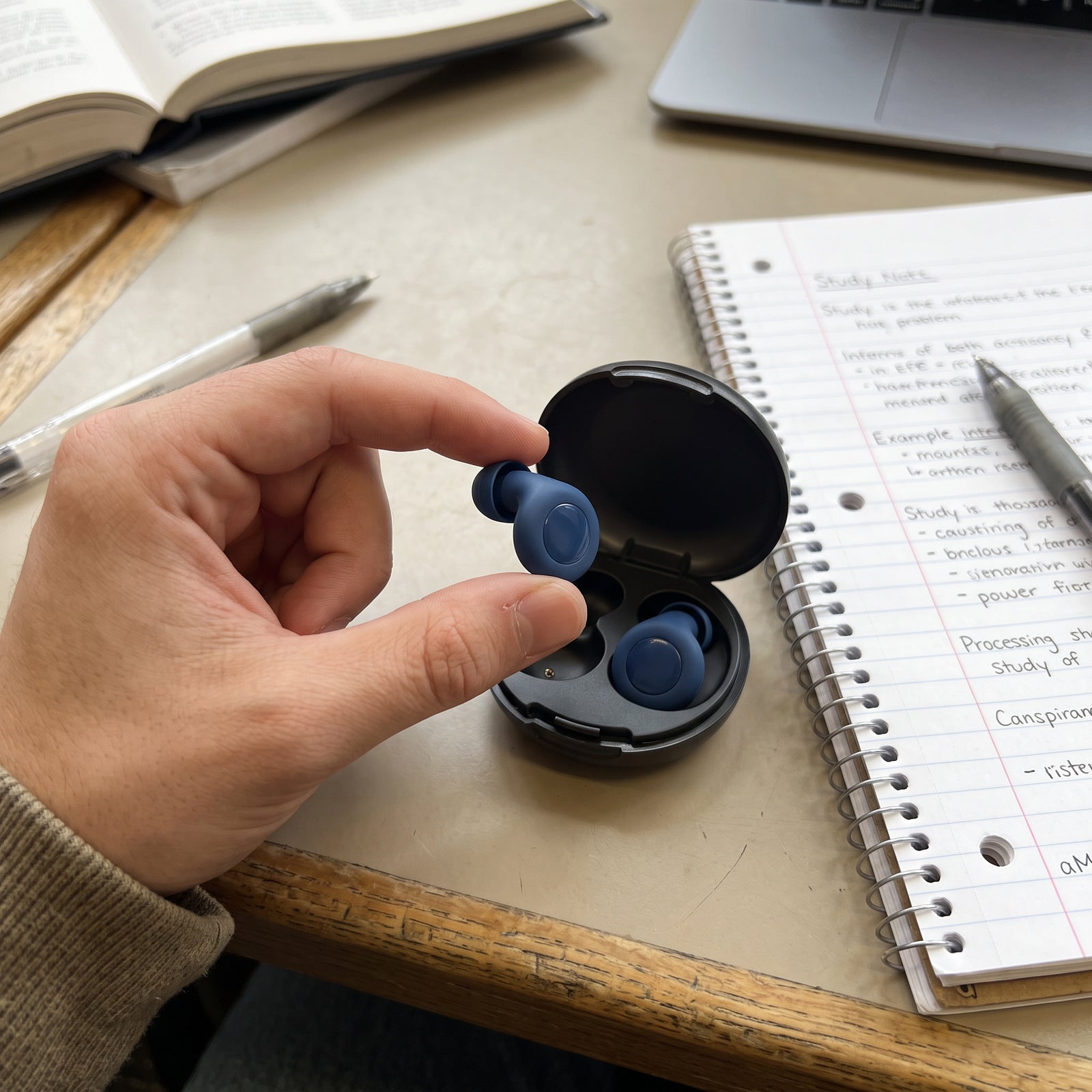 Student lifting a Blue Stillday earplug from its case at a library desk