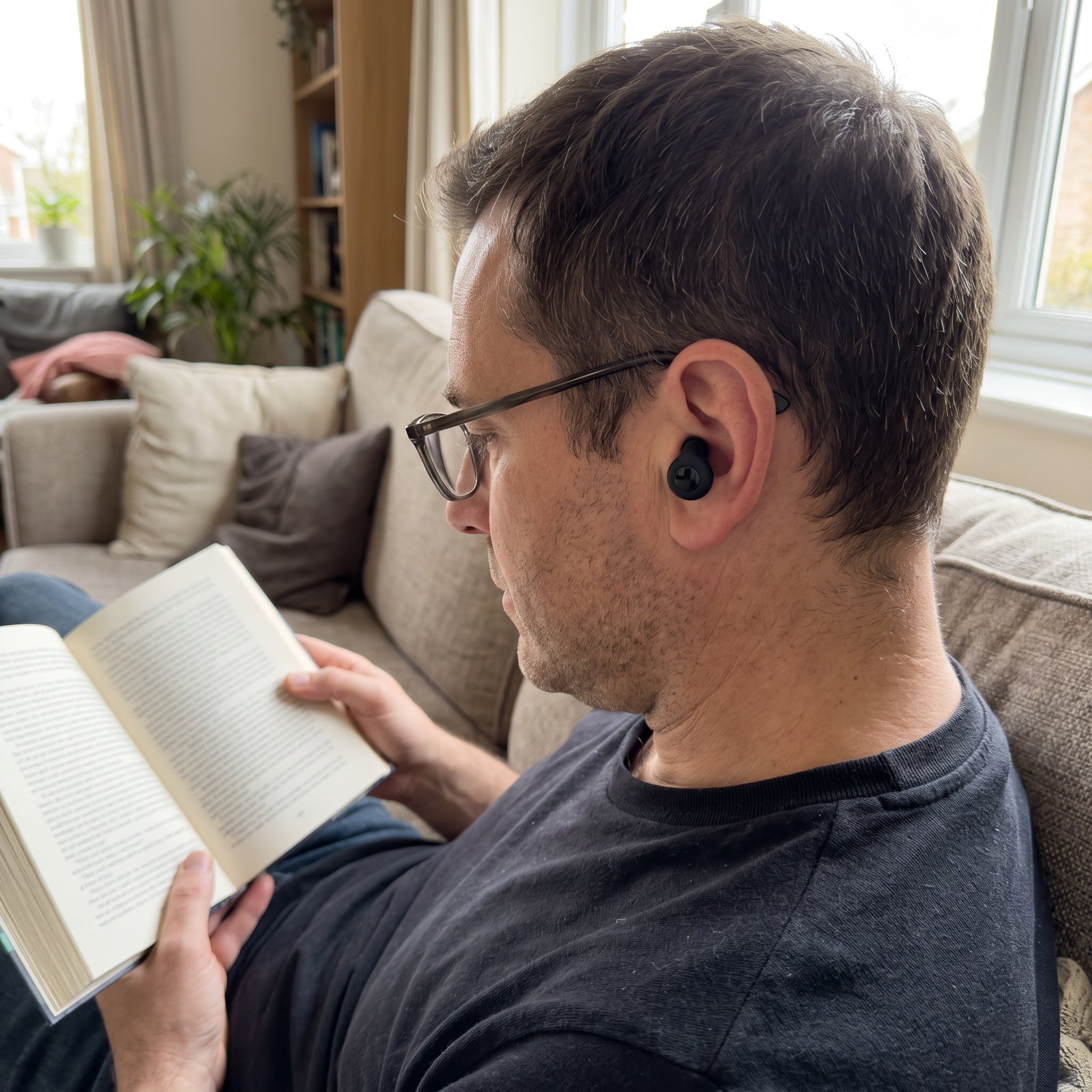 Man wearing Black Stillday earplugs while reading on his sofa
