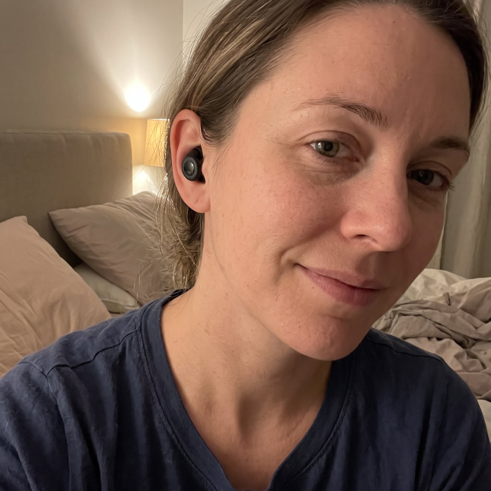 Woman in a blue nightshirt wearing Black Stillday earplugs in a bedtime selfie
