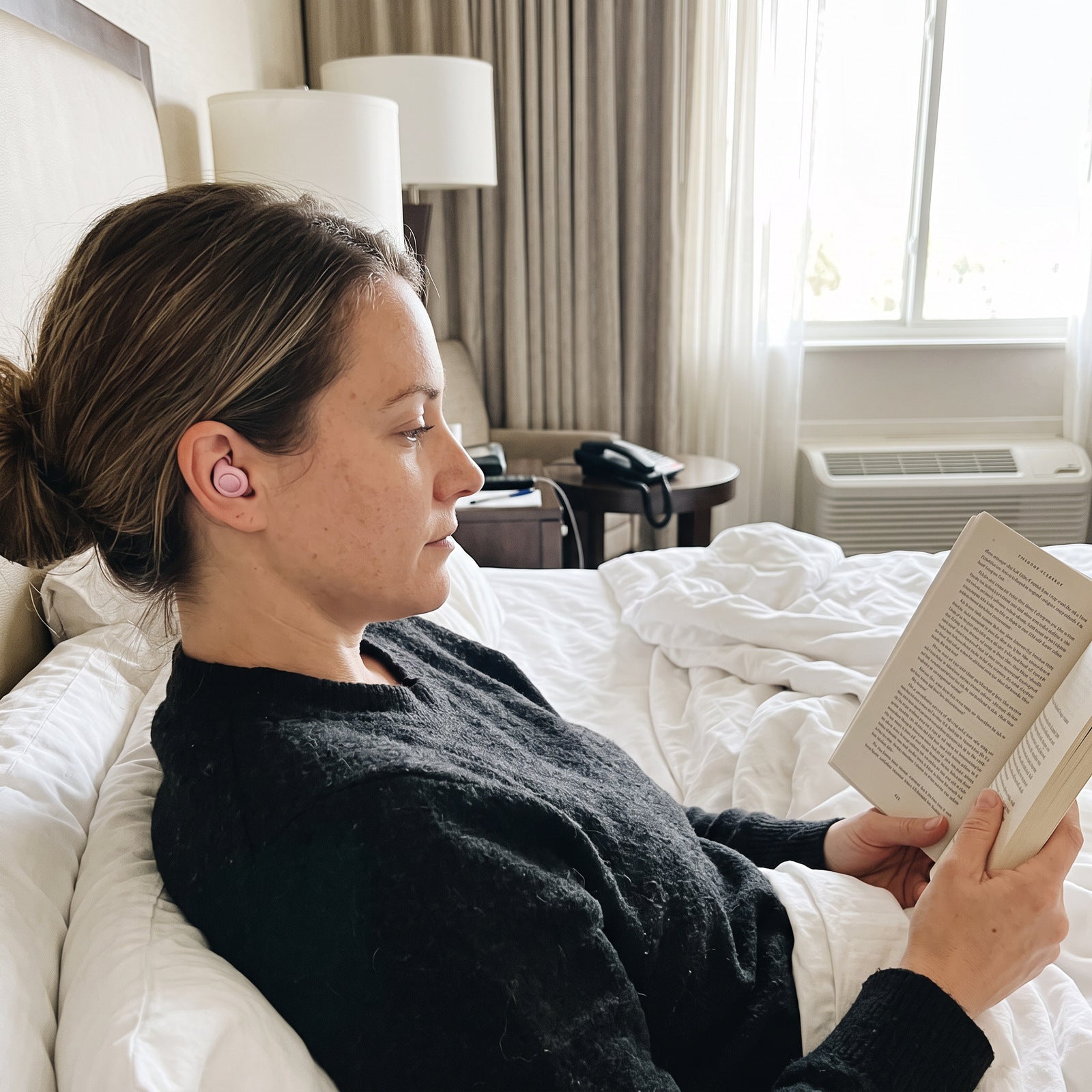 Woman wearing Pink Stillday earplugs while reading in a hotel room