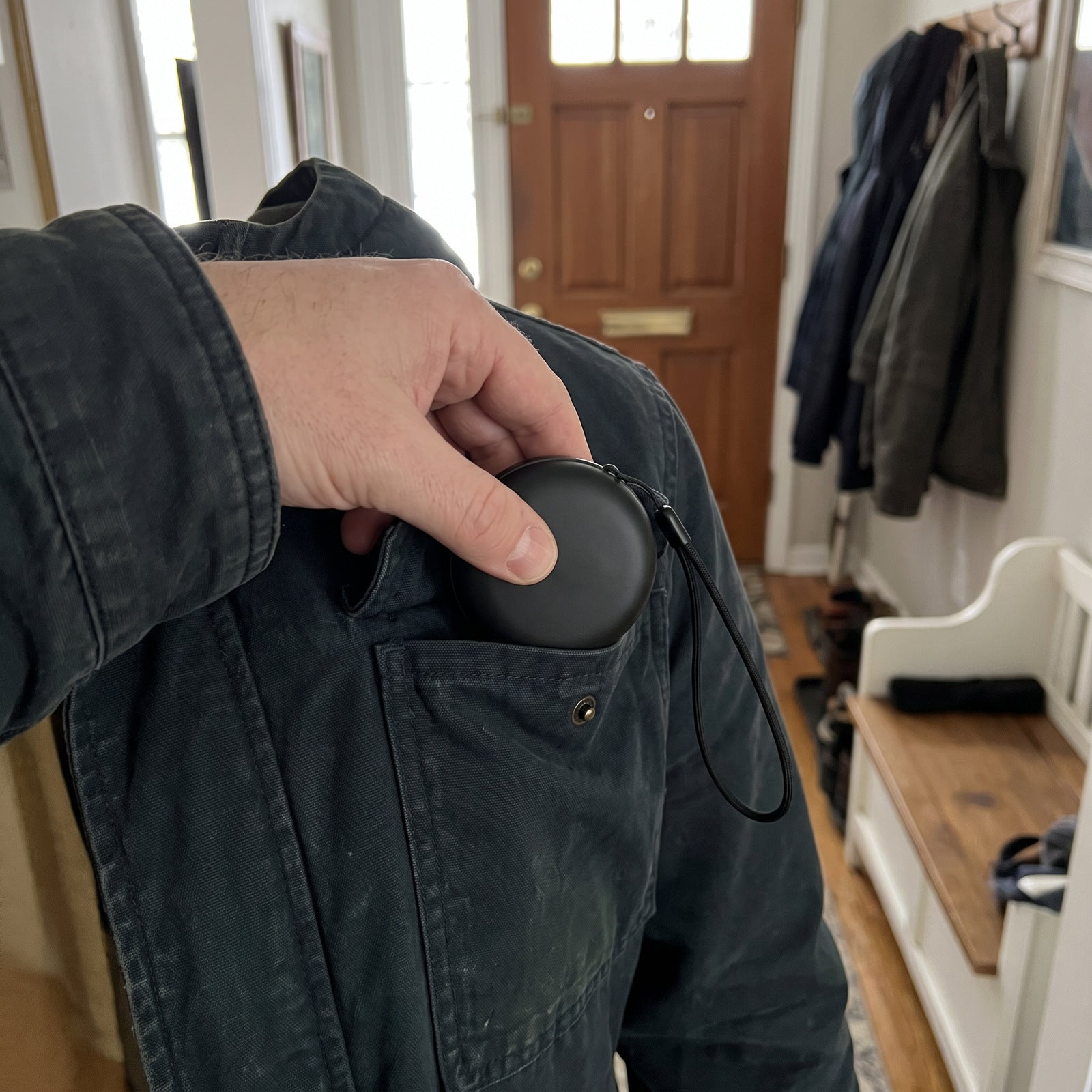Hand putting the closed round case and lanyard into a jacket pocket