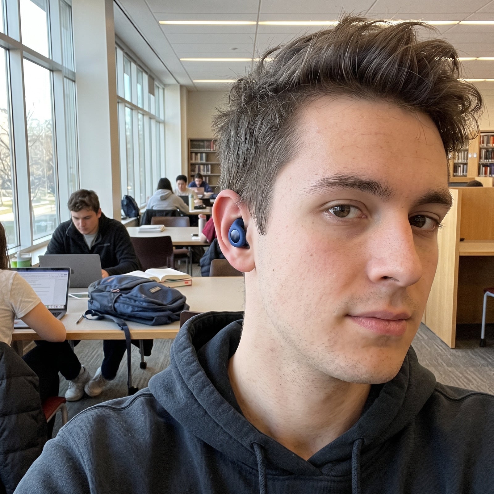 Student wearing Blue Stillday earplugs in a shared study-room selfie