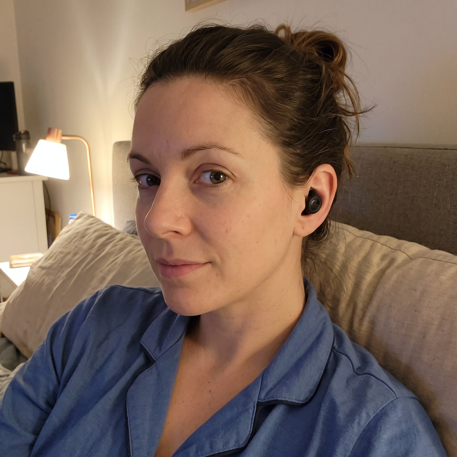 Woman in blue pyjamas wearing Black Stillday earplugs in a bedtime selfie